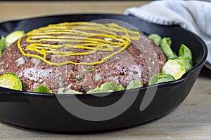 Raw meatloaf surrounded by steamed brussel sprouts in a cast iron pan ready to be baked in the oven