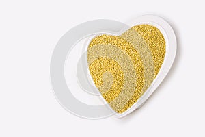 Raw millet a heart shaped plate on white background. Healthy breakfast. Organic and vegetarian food. Porridge and cereal concept.