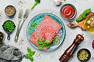 Raw mince beef, ground meat with herbs and spices on a plate.
