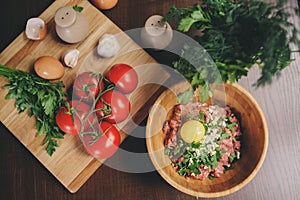 Raw minced meat with egg, herbs and fresh tomatoes on wooden table. Ingredients for cooking meat balls or loaf