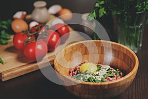 Raw minced meat with egg, herbs and fresh tomatoes on wooden table. Ingredients for cooking meat balls or loaf