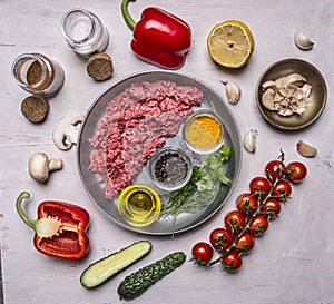Raw minced meat, half lined with pan with spices and herbs and butter, with tomatakmi on a branch, peppers, cucumbers and salt on photo