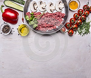 Raw minced meat with mushrooms in a pan, pepper, tomatoes on a branch, spices, cucumbers border ,text area, on wooden rustic