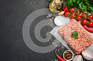 Raw minced meat on paper with fresh vegetables and spices on black background