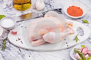 Raw mini Chicken on wooden cutting board with sea salt and different spices over old surface