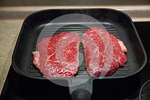 Raw minute steak of marbled beef in a grill pan on an electric cooking surface