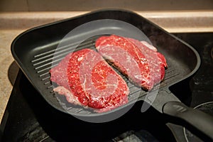 Raw minute steak of marbled beef in a grill pan on an electric cooking surface