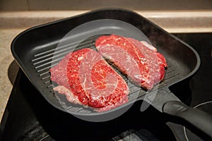 Raw minute steak of marbled beef in a grill pan on an electric cooking surface