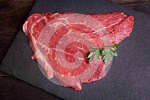 Raw minute steak of marbled beef with a parsley leaf on a stone slate board