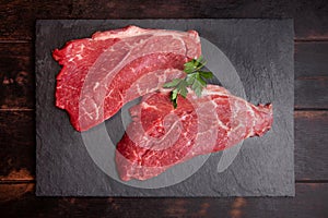 Raw minute steak of marbled beef with a parsley leaf on a stone slate board