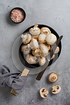 Raw mushrooms champignon in cast-iron old pan on an old concrete gray rustic background for frying. Top view