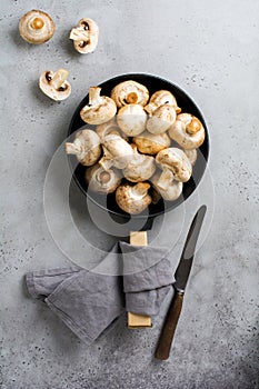 Raw mushrooms champignon in cast-iron old pan on an old concrete gray rustic background for frying. Top view