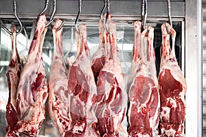 Raw mutton or lamb legs hanging on butcher hooks