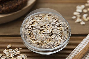 Raw oat-flakes in glass bowl on wooden spoon on wooden table