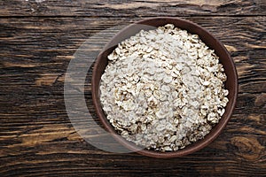 Raw oatmeal in a bowl, on a brown wooden table.