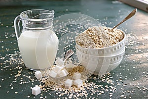 Raw Oatmeal in a glass bowl on the table, milk in a jug, sugar and spoons. Ingredients for Breakfast.