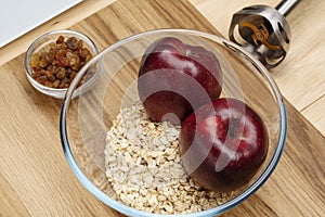 Raw oatmeal, two red apples and a blender lie on a cutting board