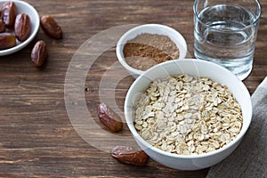 Raw oatmeal in a white bowl, dates fruits, cocoa and a glass of water, ingredients for delicious healthy breakfast