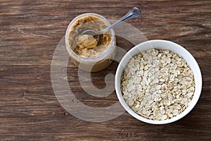 Raw oatmeal in a white bowl with peanut butter, ingredients for a delicious healthy breakfast on a wooden background