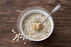 Raw oatmeal in a white bowl with peanut butter, ingredients for a delicious healthy breakfast on a wooden background