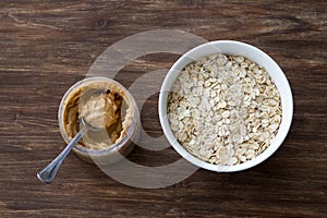 Raw oatmeal in a white bowl with peanut butter, ingredients for a delicious healthy breakfast on a wooden background