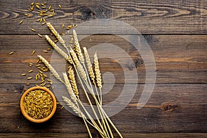 Raw oats in bowl near sprigs of wheat on dark wooden background top view copy space