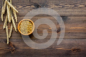Raw oats in bowl near sprigs of wheat on dark wooden background top view copy space