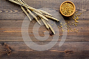 Raw oats in bowl near sprigs of wheat on dark wooden background top view copy space