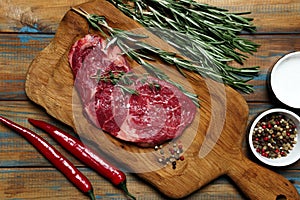 Raw organic beef meat with rosemary, seasonings, salt and red pepper on wooden cutting board