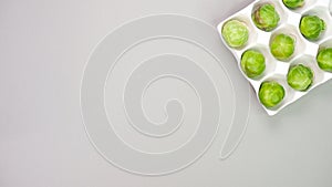 Raw organic Brussel sprouts in yellow white egg container on grey background