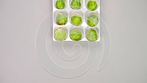 Raw organic Brussel sprouts in yellow white egg container on grey background