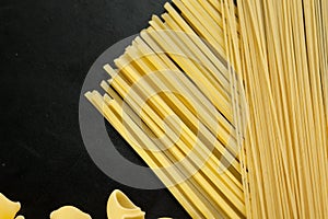 Raw organic macaroni shells and spaghetti on the black table