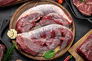 Raw organic marbled beef with spices on a wooden cutting board on a black slate, stone or concrete background