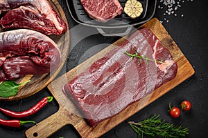 Raw organic marbled beef with spices on a wooden cutting board on a black slate, stone or concrete background