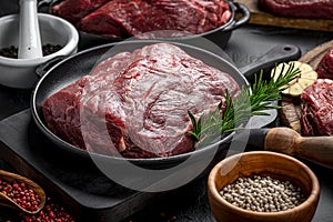 Raw organic marbled beef with spices on a wooden cutting board on a black slate, stone or concrete background