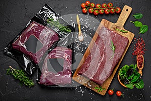 Raw organic marbled beef with spices on a wooden cutting board on a black slate, stone or concrete background