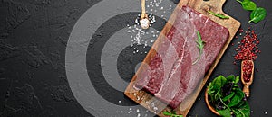 Raw organic marbled beef with spices on a wooden cutting board on a black slate, stone or concrete background