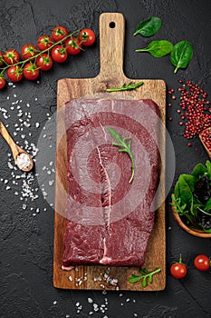 Raw organic marbled beef with spices on a wooden cutting board on a black slate, stone or concrete background