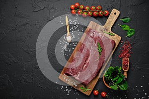 Raw organic marbled beef with spices on a wooden cutting board on a black slate, stone or concrete background