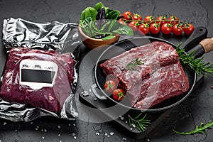 Raw organic marbled beef with spices on a wooden cutting board on a black slate, stone or concrete background