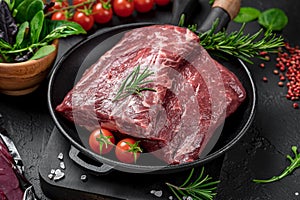 Raw organic marbled beef with spices on a wooden cutting board on a black slate, stone or concrete background