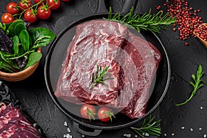 Raw organic marbled beef with spices on a wooden cutting board on a black slate, stone or concrete background