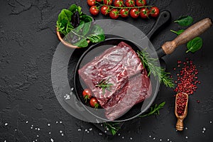 Raw organic marbled beef with spices on a wooden cutting board on a black slate, stone or concrete background