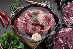 Raw organic marbled beef with spices on a wooden cutting board on a black slate, stone or concrete background