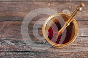 Raw organic red dried saffron spice on wooden background in vintage metal brass mortar with pestle