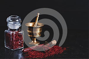 Raw organic red dried saffron spice on wooden background in vintage metal brass mortar with pestle, glass jar and tube