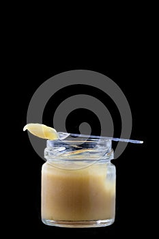 Raw organic royal jelly in a small bottle with litte spoon on black