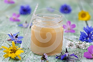 Raw organic royal jelly in a small bottle with litte spoon on small bottle surrounded by flowers