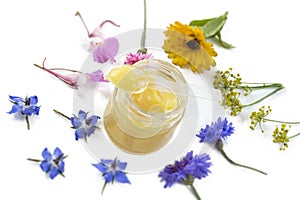 Raw organic royal jelly in a small bottle with litte spoon on small bottle surrounded by flowers on old white background