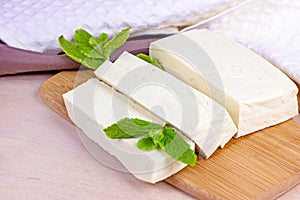 Raw organic vegetarian tofu slices with fresh mint on wooden background.